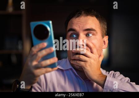 Eine Nahaufnahme eines nachdenklichen Mannes, der sein Smartphone drinnen auf einem Sofa benutzt, einen Chat liest oder online Nachrichten ansieht. Menschen, Lebensstil, drahtlose Technologie Stockfoto