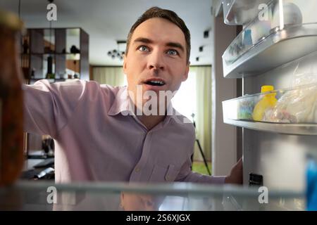 Hungriger Erwachsener kaukasischer Geschäftsmann Unternehmer Mann nach der Arbeit leeren Kühlschrank öffnen. POV-Sichtweise vom Inneren des Kühlschranks aus Stockfoto