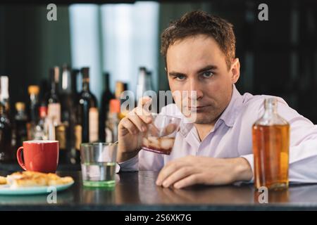 Traurige traurige junge Alkoholiker sitzen am Tisch mit einer Flasche Rum. Das Gesicht eines betrunkenen Mannes. Dumme Emotionen. Depression und Alkoholismus. Stockfoto