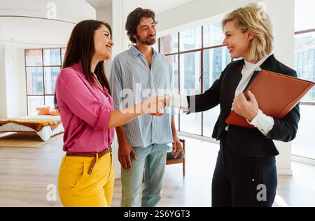Immobilienmakler zeigt einem jungen Paar eine neue Wohnung und Eigenschaften einer guten Investition. Frau und Mann kaufen ein Grundstück in einer reichen Gegend des C Stockfoto