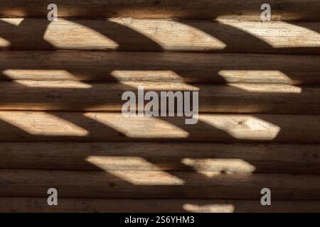 Neue Holzwand aus naturfarbenen Kiefernstämmen mit Licht- und Schattenmuster, Frontansicht, Hintergrundfotostruktur. Das Blockhaus steht unter Spannung Stockfoto