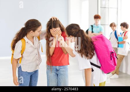 Trauriges Mädchen, das von Klassenkameraden im Schulflur gemobbt wurde, ihr Gesicht bedeckt und sich verzweifelt fühlt. Stockfoto