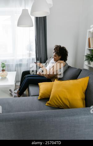 Glückliches afroamerikanisches Paar genießt eine gute gemeinsame Zeit beim Fernsehen. Mann und Frau saßen eng auf der Couch und zeigten Komfort Stockfoto