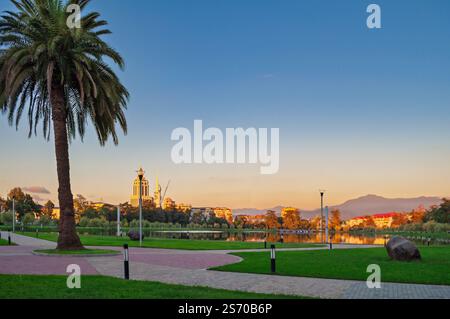 Malerischer Blick auf einen Stadtpark in Georgia mit einer Palme, Wanderwegen und architektonischen Gebäuden zur goldenen Stunde. Stockfoto
