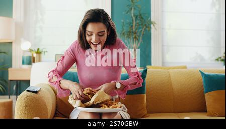 Zu Hause, Burger und Happy Woman mit Fast Food, Pommes Frites und begeistert vom Mitnehmen. Ernährung, Hamburger und Mädchen essen Mittagessen, Rindfleisch Sandwich Stockfoto