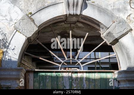 Veralteter Torbogen mit rostigem Metallgitter über verwittertem grünen Holztor. Stockfoto