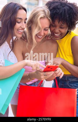 Drei fröhliche junge Frauen, die zusammen ein Smartphone ansehen. Vertikal Stockfoto