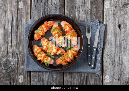 Uunimakkara, gebacken im Ofen Würstchen mit Käse, Tomaten und Senf in Backform auf grauem Holztisch mit Besteck, finnisches Rezept, horizonta Stockfoto