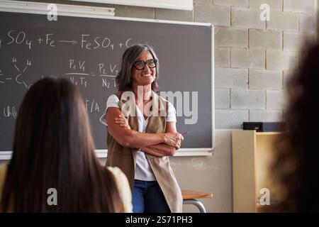 Reifer Lehrer in einem Klassenzimmer, unterrichtet Chemie, während die Schüler in einer einnehmenden Atmosphäre zuhören. Stockfoto