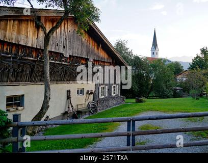 Malerische Alpenlandschaft mit einem charmanten alten Bauernhof und einer Dorfkirche im Hintergrund in Schwangau in den Bayerischen Alpen an einem ruhigen Abend Stockfoto