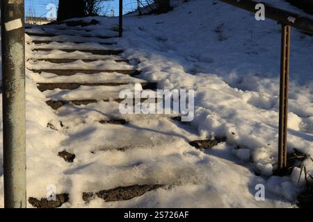 Eine Außentreppe führt hinauf, bedeckt mit Schnee und beleuchtet von der Sonne und den Schneeschwankungen an der Seite Stockfoto