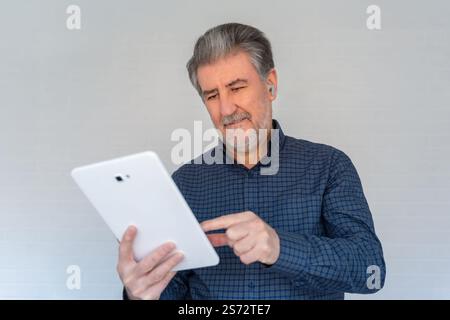Ein älterer weißer Mann, der auf ein Tablet blickt, den Bildschirm mit positiver Einstellung berührt und lächelt. Stockfoto