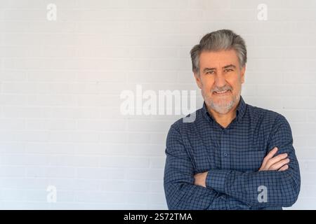 Ein älterer weißer Mann, der in die Kamera schaut, mit positiver Einstellung an einer weißen Wand mit Copysapce. Stockfoto