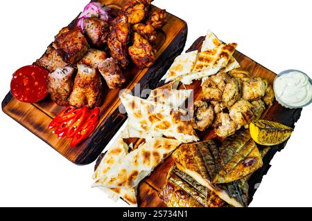 Gegrilltes Huhn, Fisch und verschiedene Fleischgerichte auf Holzbrettern, begleitet von Fladenbrot und Beilagen. Dieses lebendige Display zeigt eine Festtage-ide Stockfoto