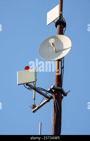 Ein hoher Stab mit einem roten Licht oben und einer weißen Satellitenschüssel unten. Der Stab besteht aus Metall und befindet sich am Himmel Stockfoto