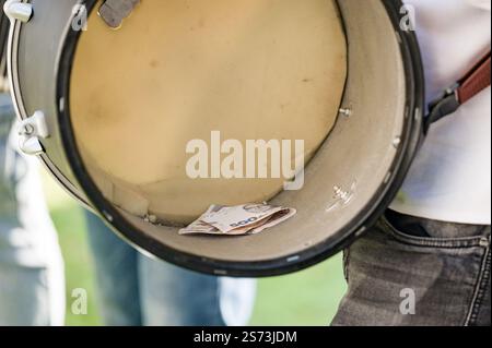 Nahaufnahme eines Trommelinneren mit gefalteten Banknoten. Die Trommel wird von einer Person gehalten, was auf Busen oder Straßenauftritte hindeutet. Stockfoto