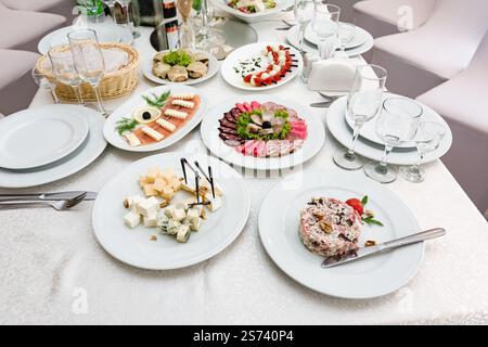 An einem sorgfältig gestalteten Buffettisch finden Sie eine Auswahl an köstlichen Vorspeisen, darunter Käse, Wurstwaren und andere Köstlichkeiten. Weiße Platten und Stockfoto