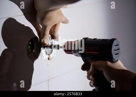 Nahaufnahme einer Hand mit einer Bohrmaschine für die elektrische Installation in einer Wand. Stockfoto