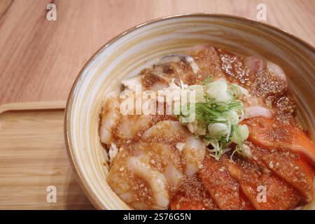 Ein wunderschön präsentierter japanischer Donburi mit frischem rohem Lachs und Jakobsmuscheln, serviert über Reis in einer Keramikschale mit Spiralmuster. Stockfoto