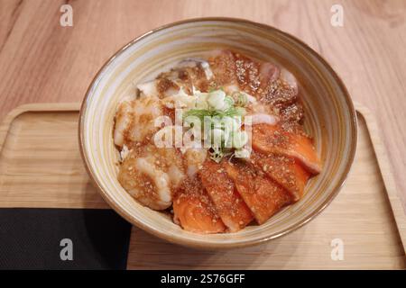Ein wunderschön präsentierter japanischer Donburi mit frischem rohem Lachs und Jakobsmuscheln, serviert über Reis in einer Keramikschale mit Spiralmuster. Stockfoto