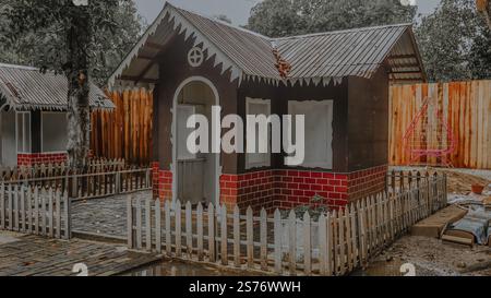 Ein kleines, dekoratives Spielhaus mit einem Pflaumenzaun mit brauner Außenseite mit weißer Zierleiste und rotem Backsteinmuster. Es befindet sich in einem Garten Stockfoto