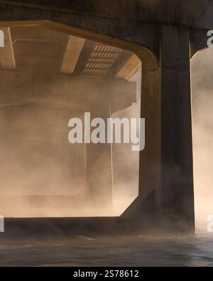 Eine kleine Brücke, die von unten gefangen wurde, in Nebel gehüllt und in warmes Morgenlicht getaucht ist. Eine ruhige und stimmungsvolle Architekturszene. Stockfoto