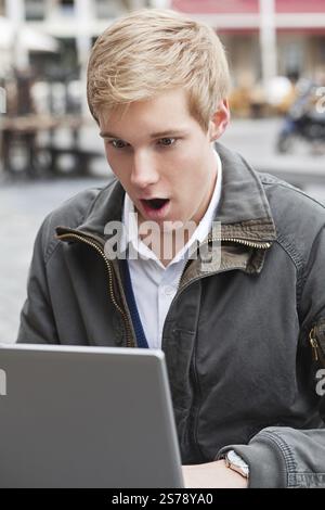 Junger gutaussehender Mann draußen, schockiert von den Informationen, die er auf dem Laptop-Bildschirm sieht, Belgien, Europa Stockfoto