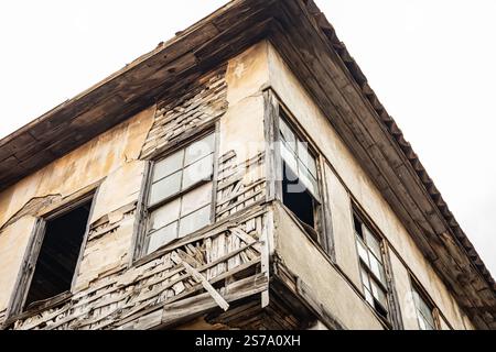 Verlassenes, verwittertes zweistöckiges Haus mit einer rissigen Holzfassade und kaputten Fenstern. Stockfoto