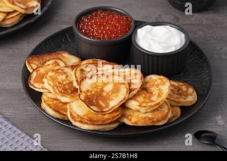 Köstlicher Stapel goldener Pfannkuchen, serviert mit Sahne und Kaviar auf einem rustikalen Tisch Stockfoto