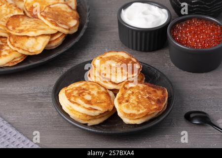 Köstlicher Stapel goldener Pfannkuchen, serviert mit Sahne und Kaviar auf einem rustikalen Tisch Stockfoto