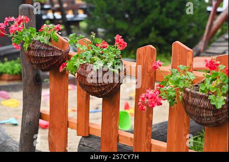 Geranienblumen in Korbkörben auf einem Holzzaun Stockfoto