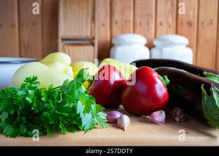 Eine Vielzahl von frischem Gemüse, einschließlich Kartoffeln, Paprika und Kräutern, ist ordentlich auf einer hölzernen Arbeitsplatte angeordnet. Diese Einstellung ist perfekt für die Zubereitung von Mahlzeiten Stockfoto