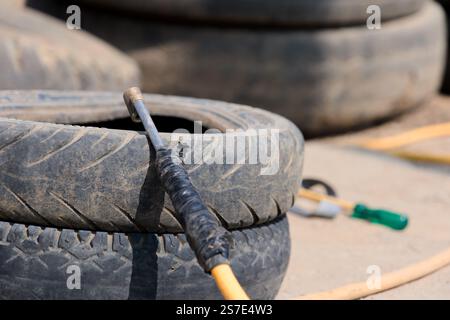 Diese Abbildung zeigt eine Nahansicht eines Stapels gebrauchter Reifen. Einer der Reifen hat eine Metallstange, die mit schwarzem Klebeband umwickelt ist Stockfoto