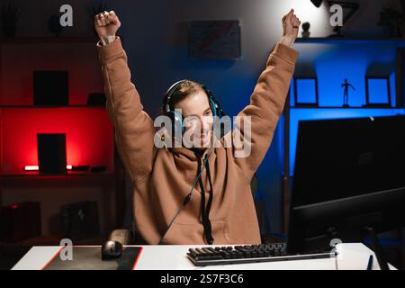 Junger kaukasischer Hipster-Profi-Gamer feiert den Sieg mit den Händen hoch und spielt nachts bei Online-Cyber-Sportspielen zu Hause. Stockfoto