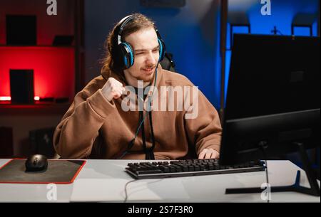 Junger kaukasischer Hipster-Pro-Gamer schreien laut yeah Fist Up Raise Win Lotterie, spielen in Online-Cyber-Sport-Spiel nachts zu Hause. Stockfoto
