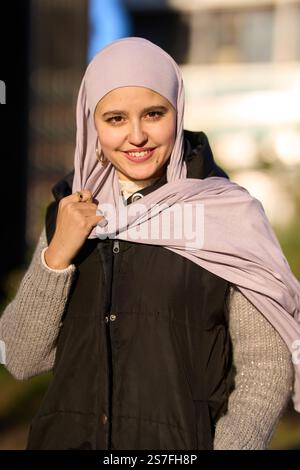 Junge muslimische Frau lächelt und hält ihren Hijab draußen Stockfoto