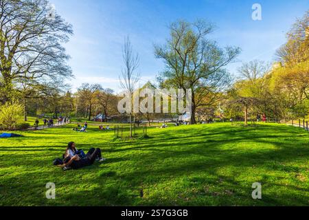 Am sonnigen Frühlingstag im Central Park mit Bäumen, Wanderwegen und Teich im Hintergrund entspannen die Menschen auf grünem Gras. New York. USA. Stockfoto