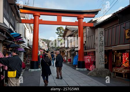 Menschen, die durch ein großes, rosa Torii Shinto-Schrein-Tor in der Nähe des Eingangs zum Fushimi Inari Taisha in Fushimi-ku, Kyoto, Japan, fahren. Stockfoto