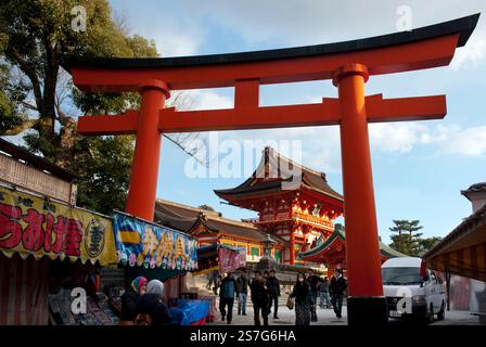 Menschen, die durch ein großes, rosa Torii Shinto-Schrein-Tor in der Nähe des Eingangs zum Fushimi Inari Taisha in Fushimi-ku, Kyoto, Japan, fahren. Stockfoto