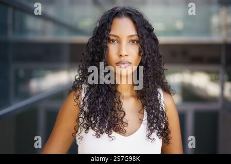 Eine selbstbewusste und lebendige junge Frau mit schönen lockigen Haaren posiert anmutig in einer urbanen Umgebung Stockfoto