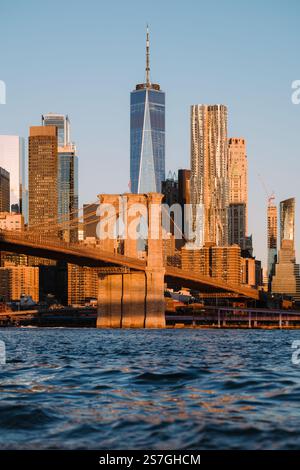 Ein atemberaubender Blick auf die Brooklyn Bridge vor dem Hintergrund der Skyline von Manhattan, die von den goldenen Tönen eines Sonnenaufgangs beleuchtet wird. Stockfoto