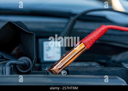 Autobatterie mit roten Überbrückungskabeln sicher befestigt, Nahaufnahme. Ladeklemme an Batterieklemme. Laden der alten Fahrzeugbatterie Stockfoto