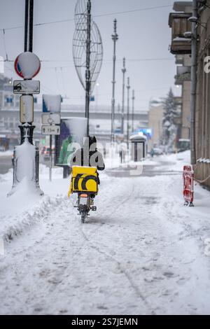 Winterservice mit Speisen. Rückansicht einer Person, die bei Schneefall mit einem Elektroroller geliefert wird Stockfoto