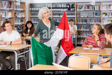 Interessante Geschichte über Mexiko, während Schüler in der Schulbibliothek unterrichtet werden. Die Lehrerin hält die Flagge Mexikos in ihren Händen Stockfoto