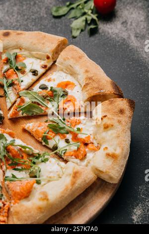 In Scheiben geschnittene Gourmet-Pizza mit Räucherlachs, Rucola und Kapern auf einem Holzbrett für ein stilvolles fest Stockfoto