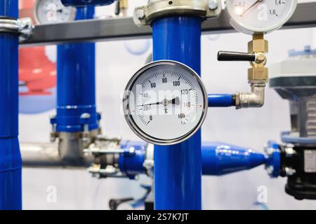 Ein blaues Rohr mit einem weiß-schwarzen Thermometer drauf. Das Thermometer zeigt eine Temperatur von 100 Grad an Stockfoto