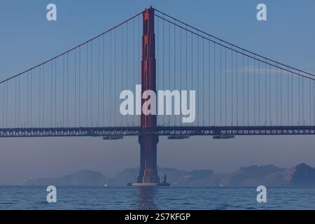 Die Golden Gate Bridge erhebt sich majestätisch vor einem klaren blauen Himmel, während tagsüber Boote auf dem Wasser darunter segeln. Stockfoto