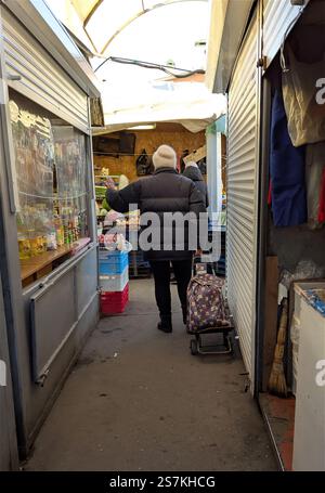 Bila Tserkva, Ukraine, 2025.01.19: Eine Großmutter mit einem Einkaufswagen läuft entlang der Marktrichtung, auf dem Wagen befindet sich eine Tasche mit Einkäufen Stockfoto