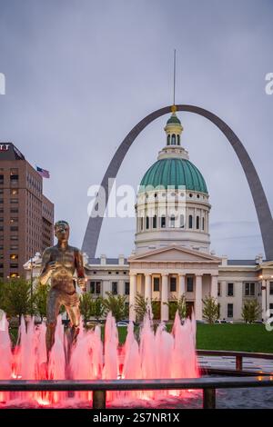 St. Louis, MO USA - 13. April 2019: Die Runner-Statue hinter dem Brunnen beleuchtet von roten Lichtern im Kienar Park mit dem Gateway Arch im Hintergrund. Stockfoto