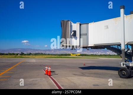 Sonnenaufgangsflugzeuge fliegen im Hintergrund, eingerahmt von einem leeren Jetway, der darauf wartet, dass das nächste Flugzeug am Flughafen Port-Au-Prince ankommt Stockfoto